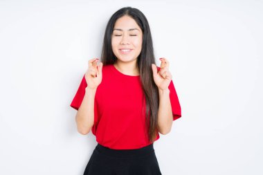 İzole arka plan üzerinde kırmızı t-shirt giyen güzel esmer kadın umut ve gözler kapalı gözleri geçiş gülümseyen. Şans ve batıl fikir.