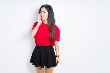 Güzel esmer kadın izole arka plan üzerinde kırmızı t-shirt ve etek giyen bağırarak ve ağızda el ile yan yüksek sesle bağırıyor. İletişim kavramı.