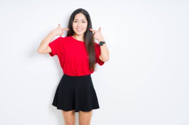 İzole arka plan üzerinde kırmızı t-shirt ve etek giyen güzel esmer kadın ve parmaklar diş ve ağız ile gösteren emin gülümseyen. Sağlık konsepti.