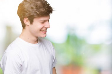 Uzak tarafına yüzünde, doğal ifade gülümseme ile seyir izole arka plan üzerinde rahat beyaz t-shirt giyen genç yakışıklı adam. Kendine güvenen gülüyor.