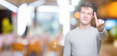 Ve parmak gülümseyen süre bir numara ile kendinden emin ve mutlu yukarıyı gösteren izole arka plan üzerinde kış kazak giyen genç yakışıklı adam.