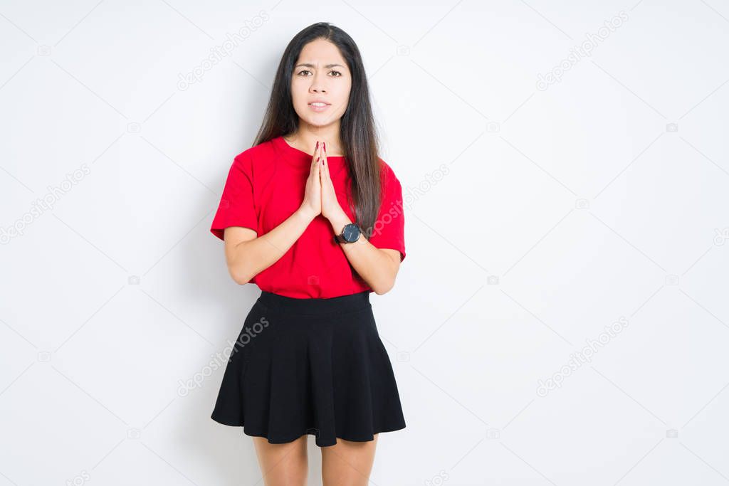 Beautiful brunette woman wearing red t-shirt and skirt over isolated background begging and praying with hands together with hope expression on face very emotional and worried. Asking for forgiveness. Religion concept.