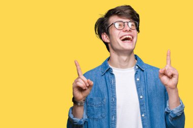 Yakışıklı delikanlı hayrete ve yukarıya bakıyor ve parmakları ile işaret ve silah kaldırdı sürpriz izole arka plan üzerinde gözlük.