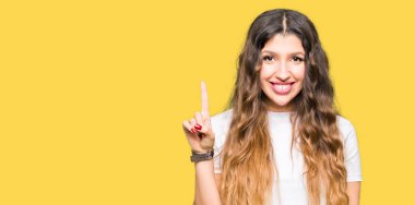 Genç güzel kadın giyiyor rahat beyaz t-shirt gösterme ve kendinden emin ve mutlu gülümseyen bir parmak ile işaret eden oktan yukarı.