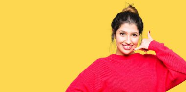 Kırmızı kazak ve çörek yapıyor gülümseyen giyen genç güzel kadın telefon hareketi ile el ve parmak telefonda konuşuyor gibi. Kavramları iletişim.