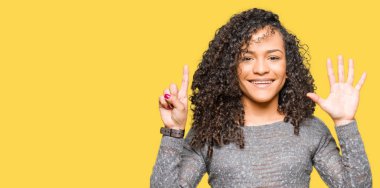 Genç güzel kadın kıvırcık saçlı giyen gri kazak gösterilen ve parmakları ile işaret ile kendinden emin ve mutlu gülümseyerek süre 6 numara.