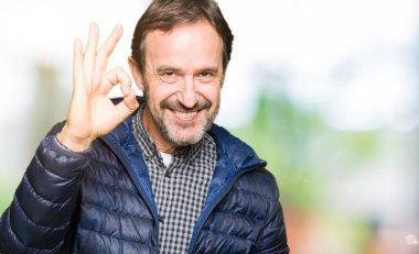 Orta yaş yakışıklı adam giyen kış ceket el ve parmaklar ok işaretiyle yapıyor olumlu gülümseyerek. Başarılı ifade.