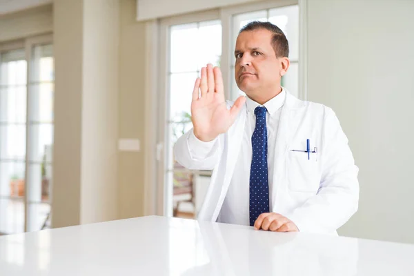 中年医生在诊所里穿着医疗服 用手掌停止唱歌 警告表情 脸上带有负面和严肃的手势 — 图库照片