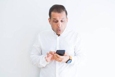 Orta yaş adam beyaz duvar üzerinde akıllı kullanarak sürpriz bir yüz ile şok korkuyor ve korku ifadesi ile heyecanlı korkmuş