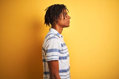 Afro Amerikan adam dreadlocks ile izole sarı arka plan üzerine çizgili gömlek giyiyor yan arıyorum, rahat bir gülümseme ile doğal yüz ile profil poz rahatlayın.