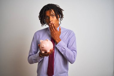 Afro Amerikan işadamı dreadlocks ile izole beyaz arka plan kapağı ağız üzerinde el ile hata için utanç ile şok, korku ifade, sessizlik, gizli kavramı korkuyor ile piggybank tutan