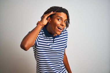 Dreadlocks ile Afro adam izole beyaz arka plan üzerinde kulak üzerinde el ile gülümseyen bir işitme söylenti veya dedikoduyu dinlerken üzerinde çizgili mavi polo ayakta giyiyor. Sağırlık konsepti.