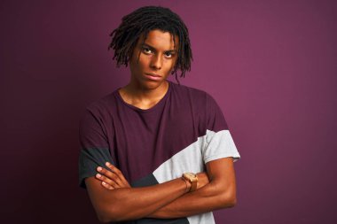 Koyu mor arka plan üzerinde ayakta rahat t-shirt giyen dreadlocks ile Afro adam şüpheci ve sinir, Çapraz kollar ile yüz ifade onaylanmaz. Negatif kişi.