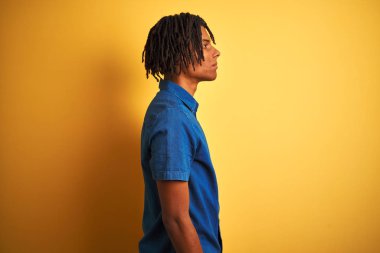 İzole sarı arka planda ayakta rahat denim gömlek dikilerek dreadlocks ile Afro adam yan arıyorum, emin gülümseme ile doğal yüz ile profil poz rahatlayın.