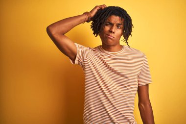 İzole sarı arka plan üzerinde duran çizgili t-shirt giyen dreadlocks ile Afro adam karıştırmayın ve soru hakkında merak. Şüpheyle belirsiz, eliyle kafada düşünmek. Pensive kavramı.