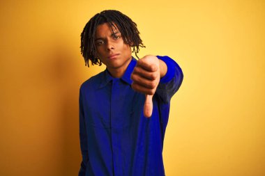 Issız sarı arka plan üzerinde mekanik üniforma giyen dreadlocks ile Afro işçi adam mutsuz ve öfkeli gösteren reddetme ve başparmak aşağı jest ile negatif bakıyor. Kötü ifade.