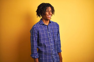 Sevimli ifade, neşeli ve mutlu yüz ile kamera bakarak izole sarı arka plan üzerinde ayakta sıradan gömlek giyen dreadlocks ile Afro adam.