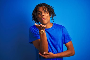 Sevimli ve seksi olmak havada elle bir öpücük üfleme kamera bakıyor izole mavi arka planda ayakta t-shirt giyen dreadlocks ile Afro Amerikan adam. Aşk ifadesi.