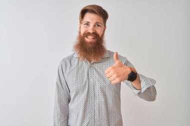 Genç Kızıl saçlı İrlandalı adam rahat gömlek ayakta giyerek izole beyaz arka plan yapıyor mutlu başparmak yukarı jest ile el. Başarı göstererek kameraya bakarak ifadeyi onaylama.