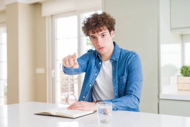 Genç adam evde kamera parmak ile işaret eden bir kitap okuma ve size, el işareti, ön olumlu ve emin jest