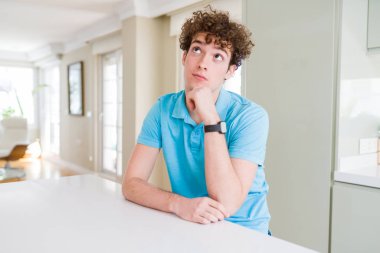 Genç yakışıklı adam rahat mavi t-shirt evde el çenesi ile soru hakkında düşünme, dalgın ifade giyiyor. Düşünceli bir yüz ile gülümsüyor. Şüphe kavramı.