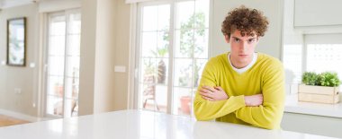 Evde Genç yakışıklı adamın geniş açı çekim şüpheci ve sinir, kesişen kollar ile yüz üzerine ifade onaylamaz. Negatif kişi.