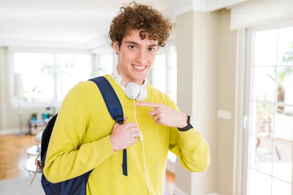 年轻的学生男子戴着耳机和背包很高兴指着手和手指 — 图库照片