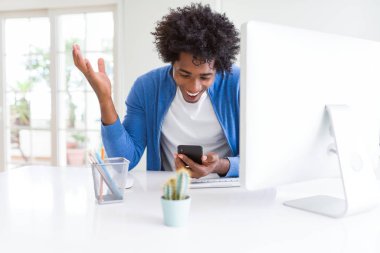 Afrika Amerikan adam akıllı telefon ve bilgisayar kullanarak çalışan çok mutlu ve heyecanlı, kazanan ifade zafer büyük gülümseme ile çığlık kutluyor ve el kaldırdı