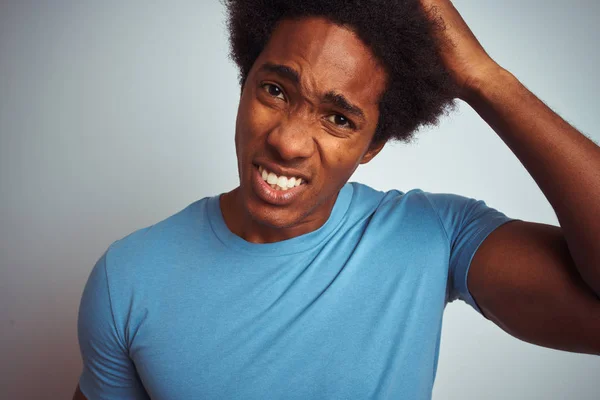 African american man with afro hair wearing blue t-shirt standing over isolated white background stressed with hand on head, shocked with shame and surprise face, angry and frustrated. Fear and upset for mistake.