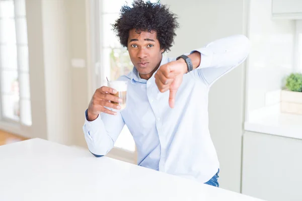 African American man with afro hair drinking a cup of coffee with angry face, negative sign showing dislike with thumbs down, rejection concept