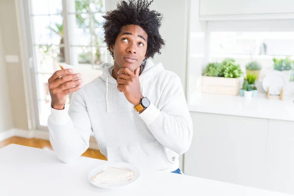 Uomo Afroamericano Mangiare Panino Fatto Mano Casa Faccia Seria Pensando — Foto Stock