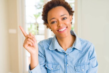 Yüzünde kocaman bir gülümseme ile genç güzel Afrikalı-Amerikalı kadın kameraya bakarak yan el ve parmak ile işaret.