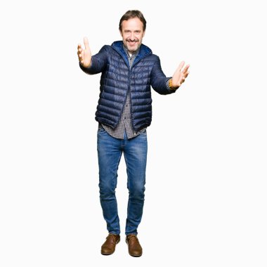 Orta yaş yakışıklı adam sarılmak için kollarını açarak gülümseyerek kameraya bakarak kış palto giyiyor. Neşeli ifade kucaklayan mutluluk.