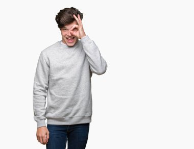 Genç yakışıklı sportif adam gülümsüyor, parmakları ile mutlu yüz üzerinden seyir göz el ile ok jest yapıyor izole arka plan üzerinde Sweatshirt giyiyor.