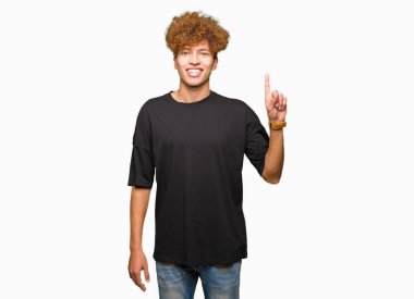 Genç yakışıklı adam ile afro saç giyen siyah t-shirt gösteren ve işaret yukarıya ile parmak sayı bir süre gülümseyen emin ve mutlu.