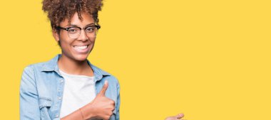 Güzel genç Afro-Amerikan kadın izole arka plan gösteren palm el ve iş tamam jestle üzerinde başparmak yukarı, gülümseyen mutlu ve neşeli gözlüklü