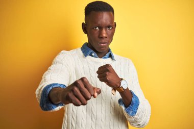 Kot gömlek giyen Afrikalı Amerikan adam ve izole sarı arka plan üzerinde beyaz kazak mücadele için yumruk Punch, agresif ve öfkeli saldırı, tehdit ve şiddet