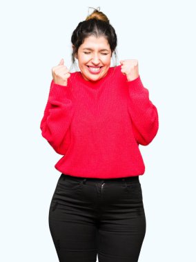 Kırmızı kazak ve çörek silah ile başarı için heyecanlı giyen genç güzel kadın kutluyor zafer gülümseyen kaldırdı. Kazanan kavramı.