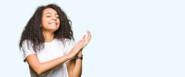 Rahat beyaz t-shirt giyen kıvırcık saç ile genç güzel kız alkışlamak ve mutlu ve neşeli, gülümseyen gururlu eller alkışladı