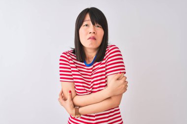 Genç güzel Çinli kadın izole beyaz arka plan üzerinde kırmızı çizgili t-shirt giyen sallayarak ve yüzünde üzgün ve şok ifade ile kış soğuk için donma