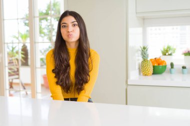 Genç güzel kadın evde beyaz masada komik surat ile yanakları şişirme. Ağız ile hava, deli ifade şişirilmiş.