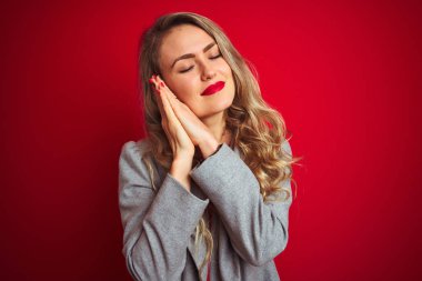 Genç güzel iş kadını kırmızı izole arka plan üzerinde duran zarif ceket giyen yorgun rüya ve kapalı gözlerle gülümseyerek birlikte elleri ile poz.