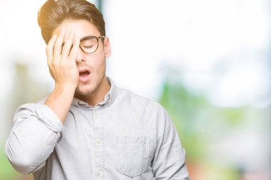 Yarım yüz, göz ve ağız el ile kapsayan yorgun esneme izole arka plan üzerinde gözlük takan yakışıklı delikanlı. Acı yüzü acıyor.