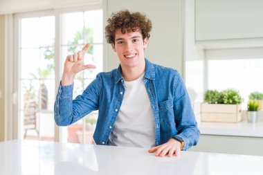 Genç yakışıklı adam evde rahat denim ceket giyiyor gülümseyen ve emin el ile boyut işareti yaparken parmaklar ile görünümlü ve kamera bakıyor. Ölçü kavramı.