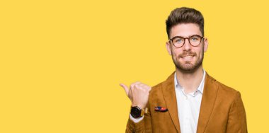 Seyir ve başparmak yanında yukarıyı mutlu yüz ile gülümseyen gözlüklü genç yakışıklı iş adamı.