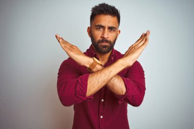 İzole gri arka plan üzerinde ayakta kırmızı zarif gömlek giyen genç Hintli adam ret ifadesi geçiş silah negatif işareti, öfkeli yüz yapıyor