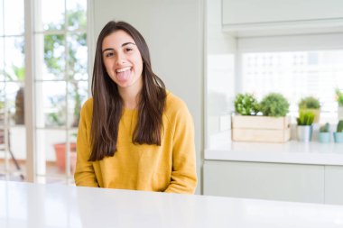 Sarı kazak giyen güzel genç kadın komik ifade ile mutlu dil yapışması. Duygu konsepti.