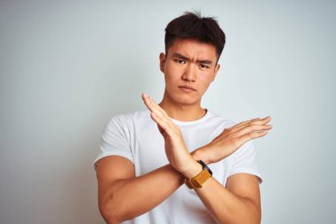 Genç Asya Çinli adam giyen t-shirt ayakta üzerinde izole beyaz arka plan ret ifadesi geçiş kolları negatif işareti, öfkeli yüz yapıyor