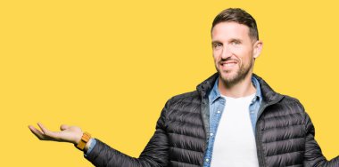 Gülen iki elle gösterilen avuç içi, sunma ve karşılaştırma ve denge reklam açık kış ceket giyen yakışıklı adam