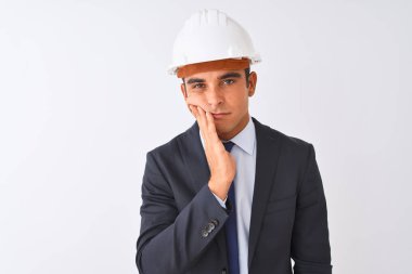 Genç yakışıklı mimar adam izole beyaz arka plan üzerinde takım elbise ve kask giyen yorgun görünümlü ve çapraz kolları ile depresyon sorunları ile sıkılmış düşünme.